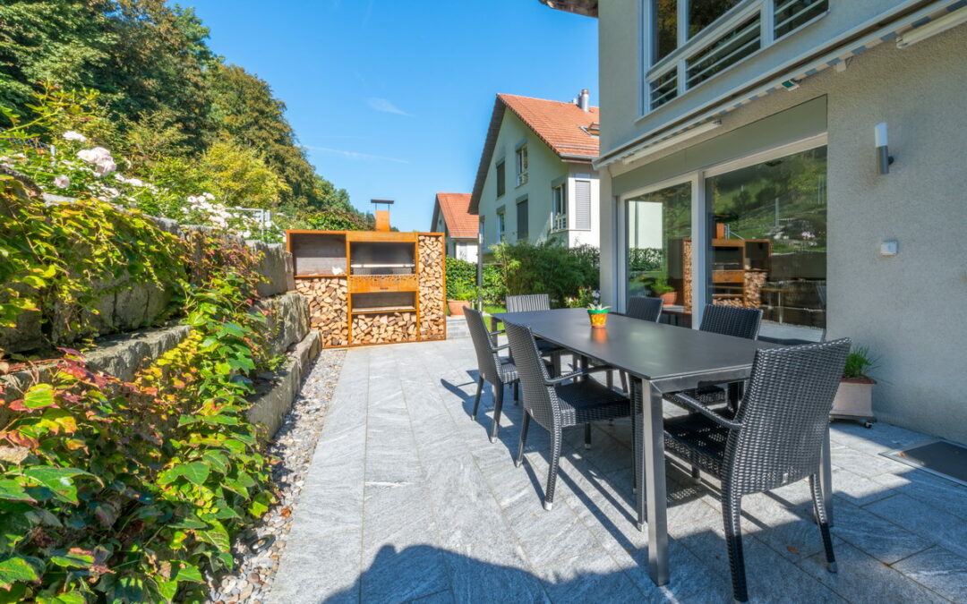 Ein Gartentisch aus Metall mit Stühlen und einem Holzlager im Hintergrund auf einer Terrasse.