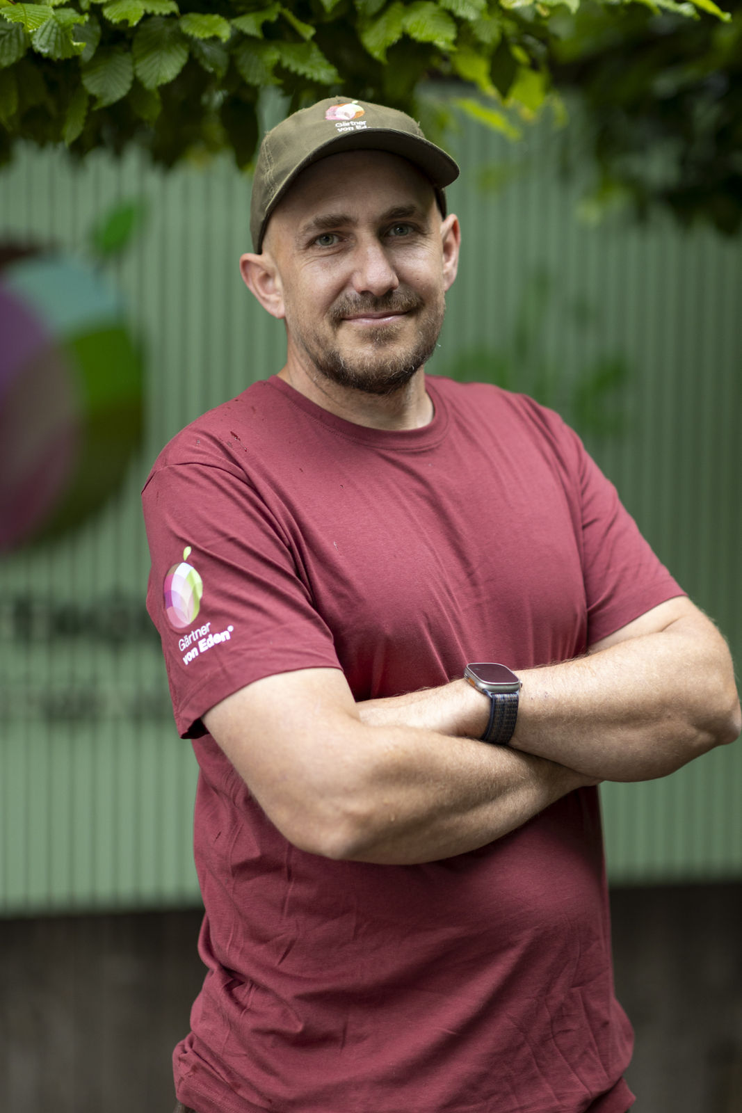 Mike Rüegg im roten Gärtner-von-Eden-Shirt vor grünem Gartenzaun Mike Rüegg, Team Gartenliebhaber, Gärtner von Eden