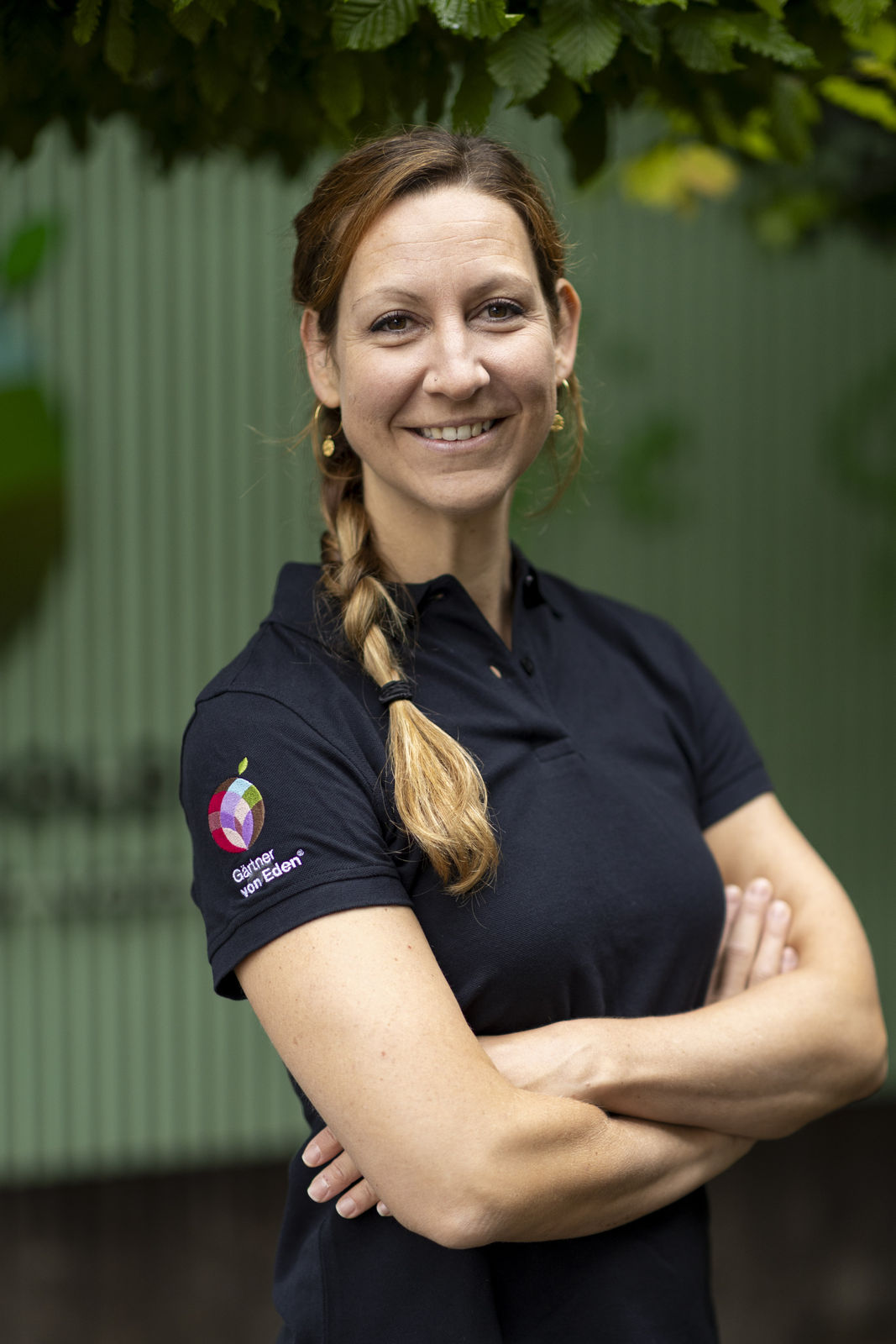 Nicole Bochsler im schwarzen Poloshirt mit Gärtner von Eden Logo, Porträt im Grünen Nicole Bochsler, Team Leuthold, in Arbeitskleidung; Leuthold Gärtner von Eden